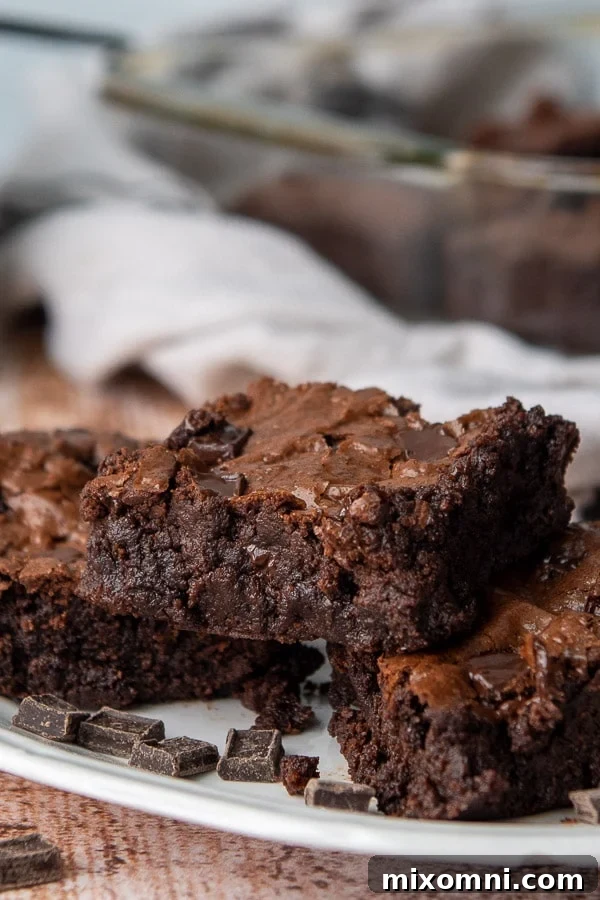A stack of three rich, fudgy almond flour brownies on a white plate, showcasing their moist interior and crackly tops.