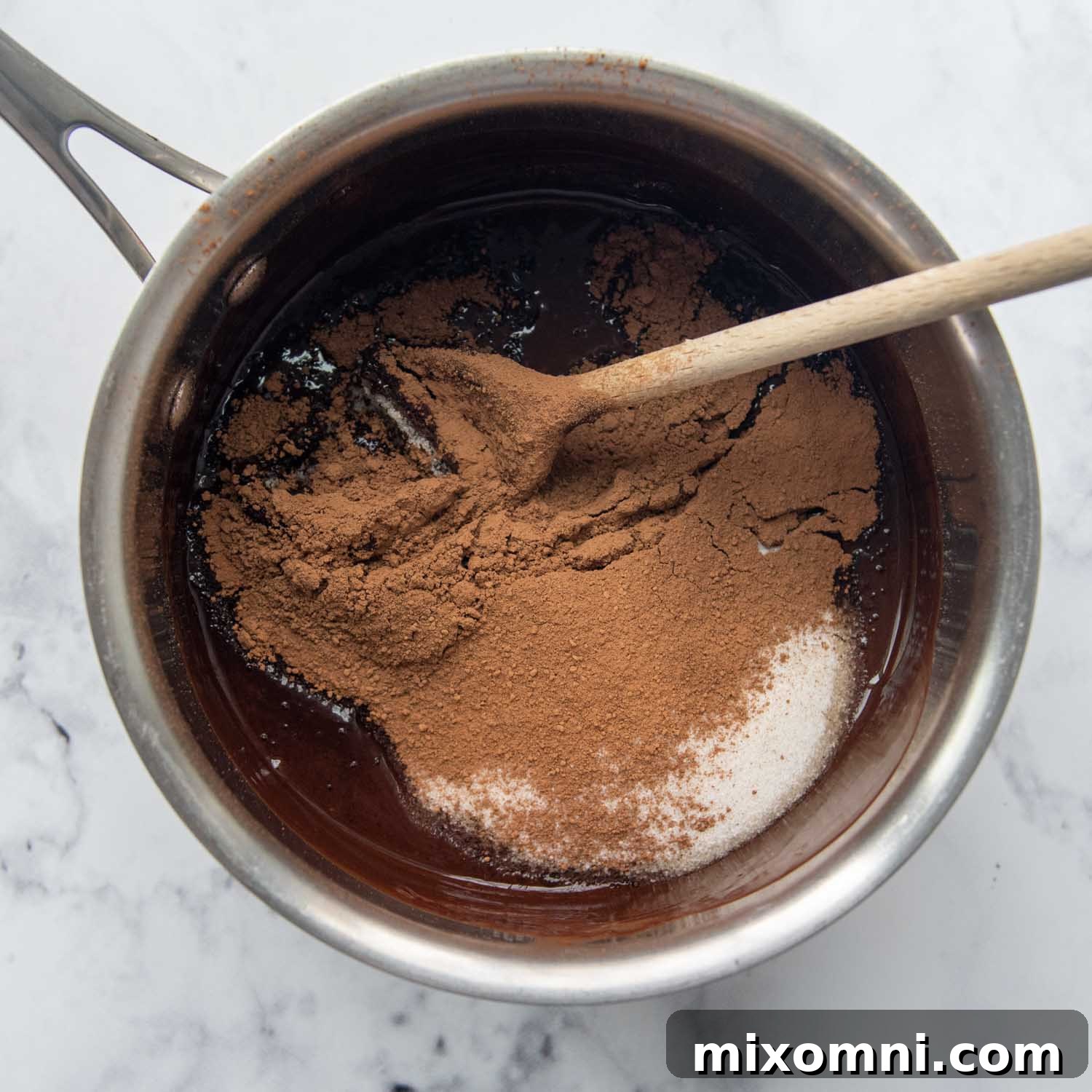 Granulated sugar and unsweetened cocoa powder being stirred into the melted butter and chocolate mixture in the pot.