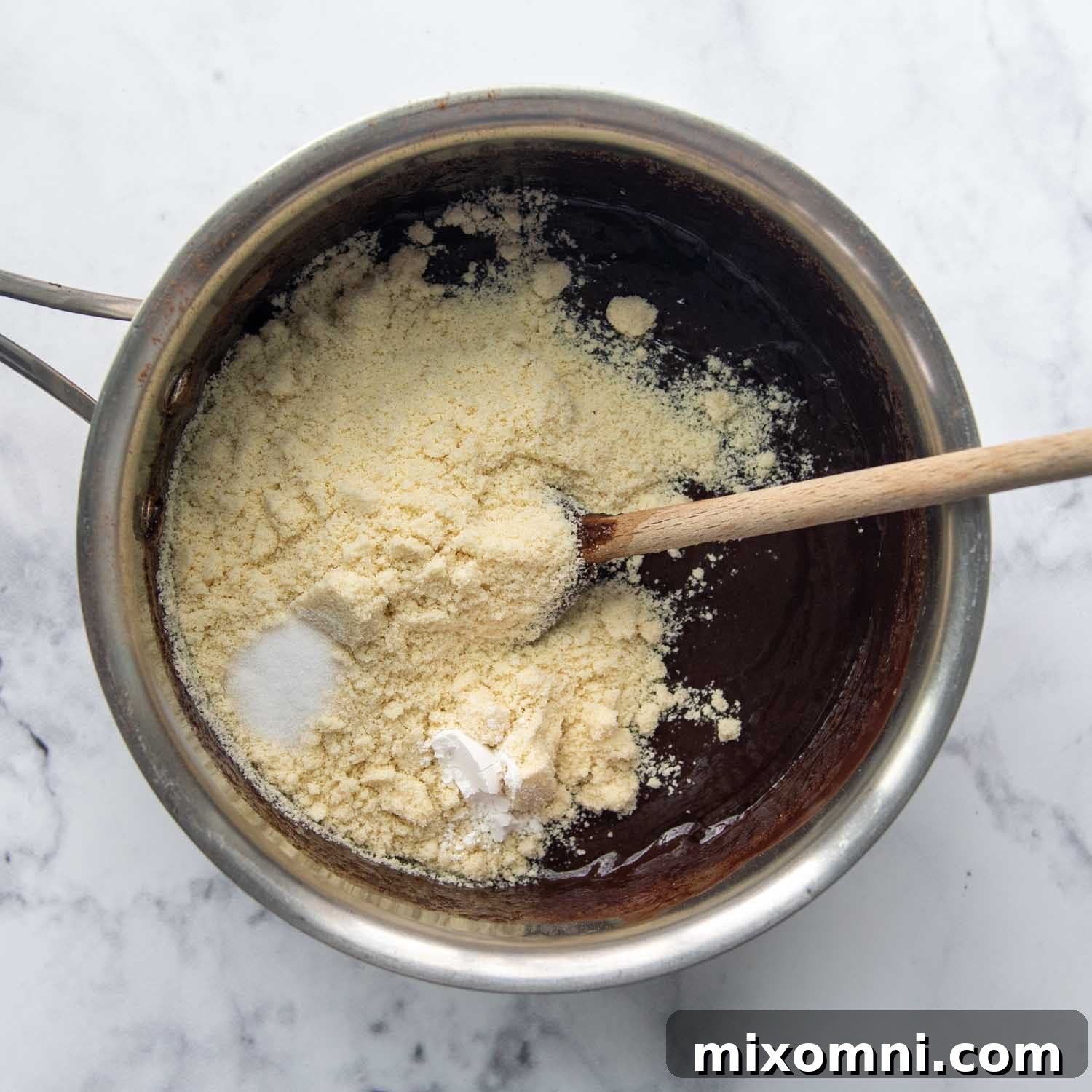 Blanched almond flour being added to the thick chocolate batter in the saucepan, ready for final mixing.