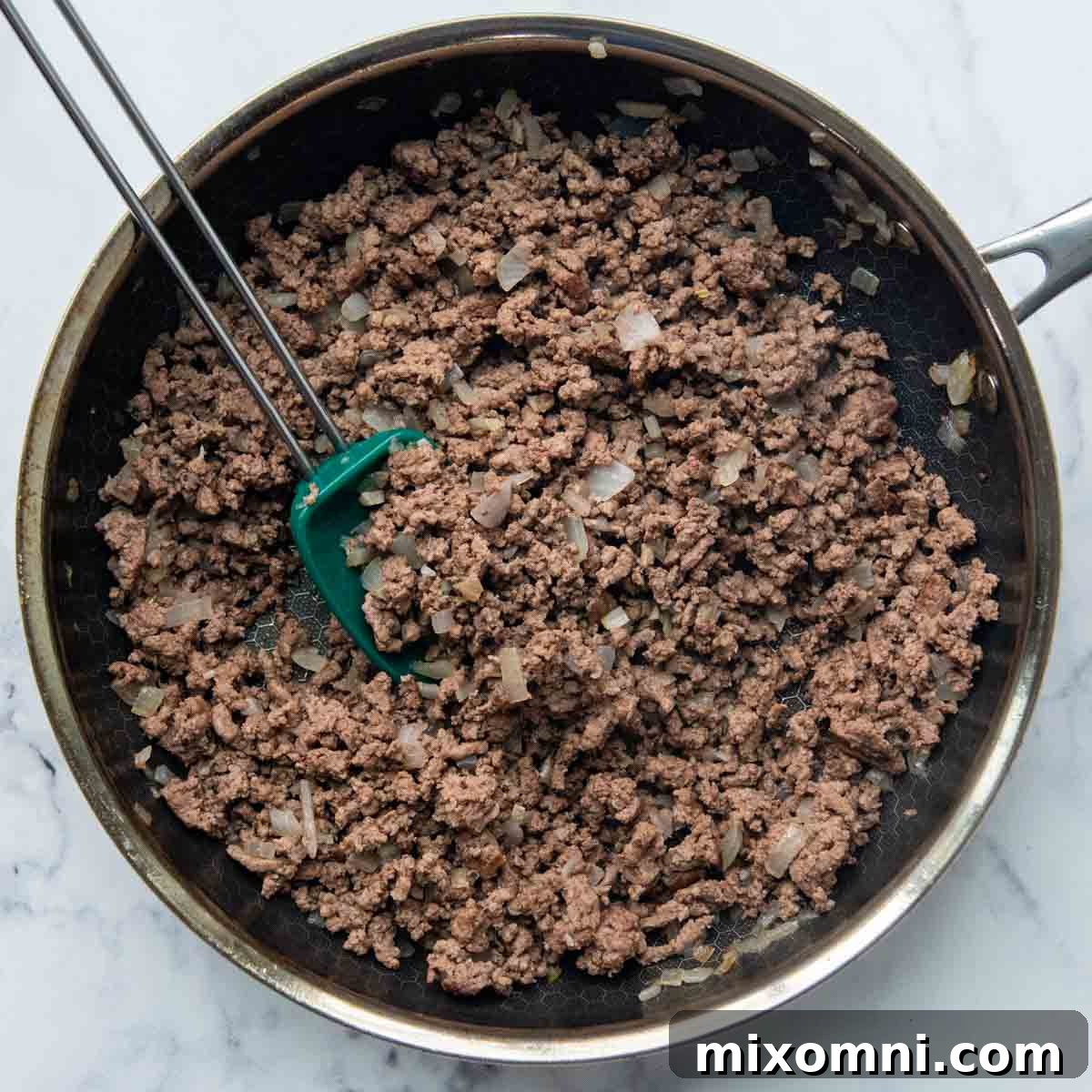 Ground beef browned with chopped onions and minced garlic in a skillet.