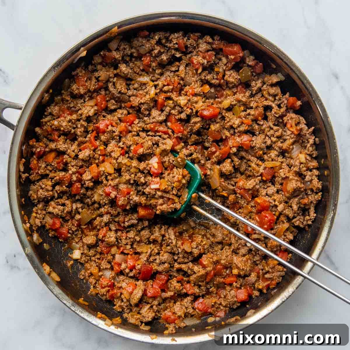 Diced tomatoes with chilies and taco seasoning added to the browned beef mixture in a skillet.