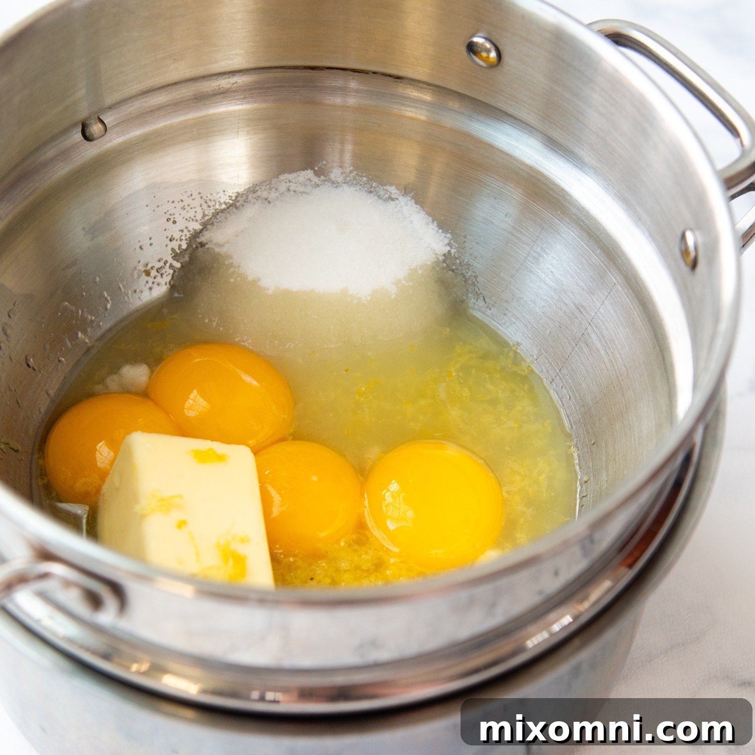 Ingredients for lemon curd being gently heated in a double boiler, showing the process of thickening.