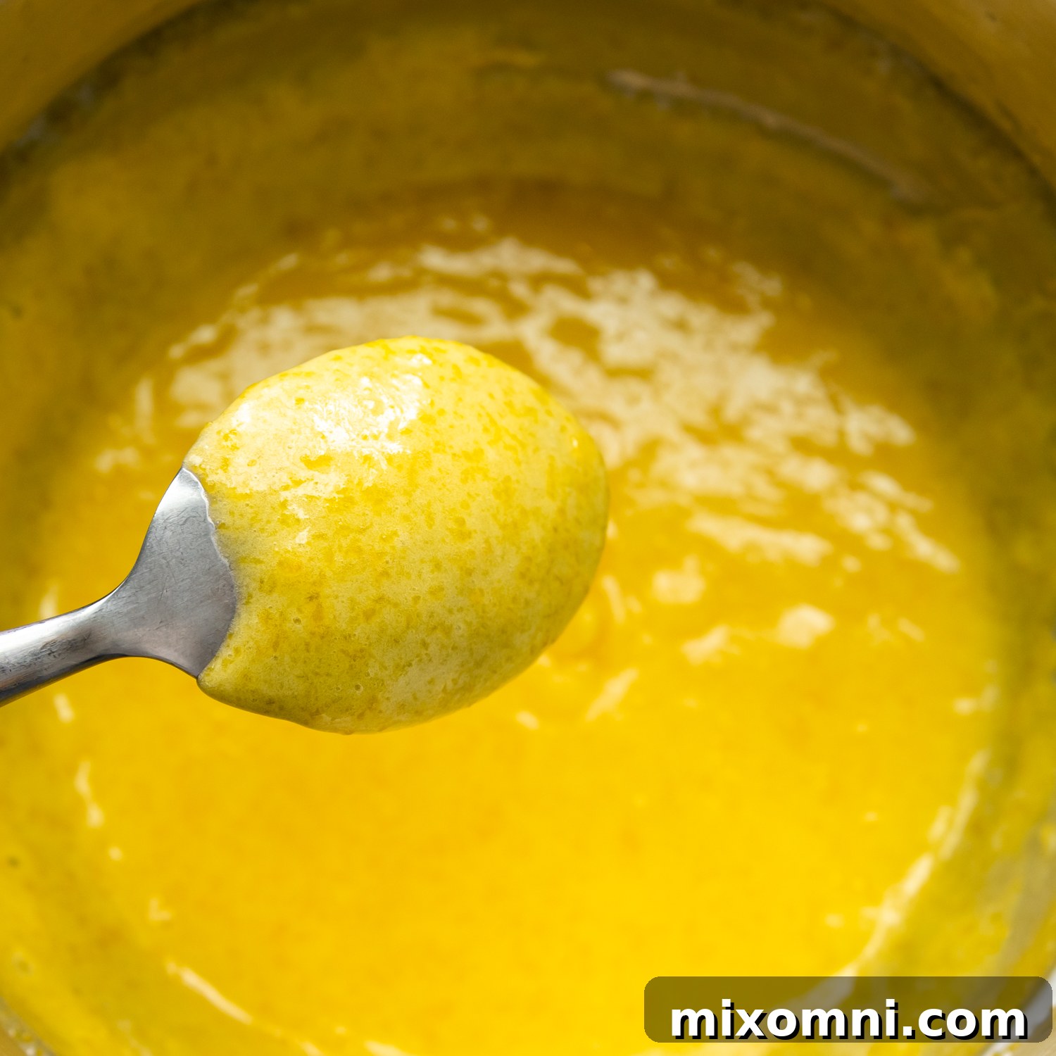 Perfectly cooked lemon curd generously coating the back of a spoon, indicating the ideal thickened consistency.