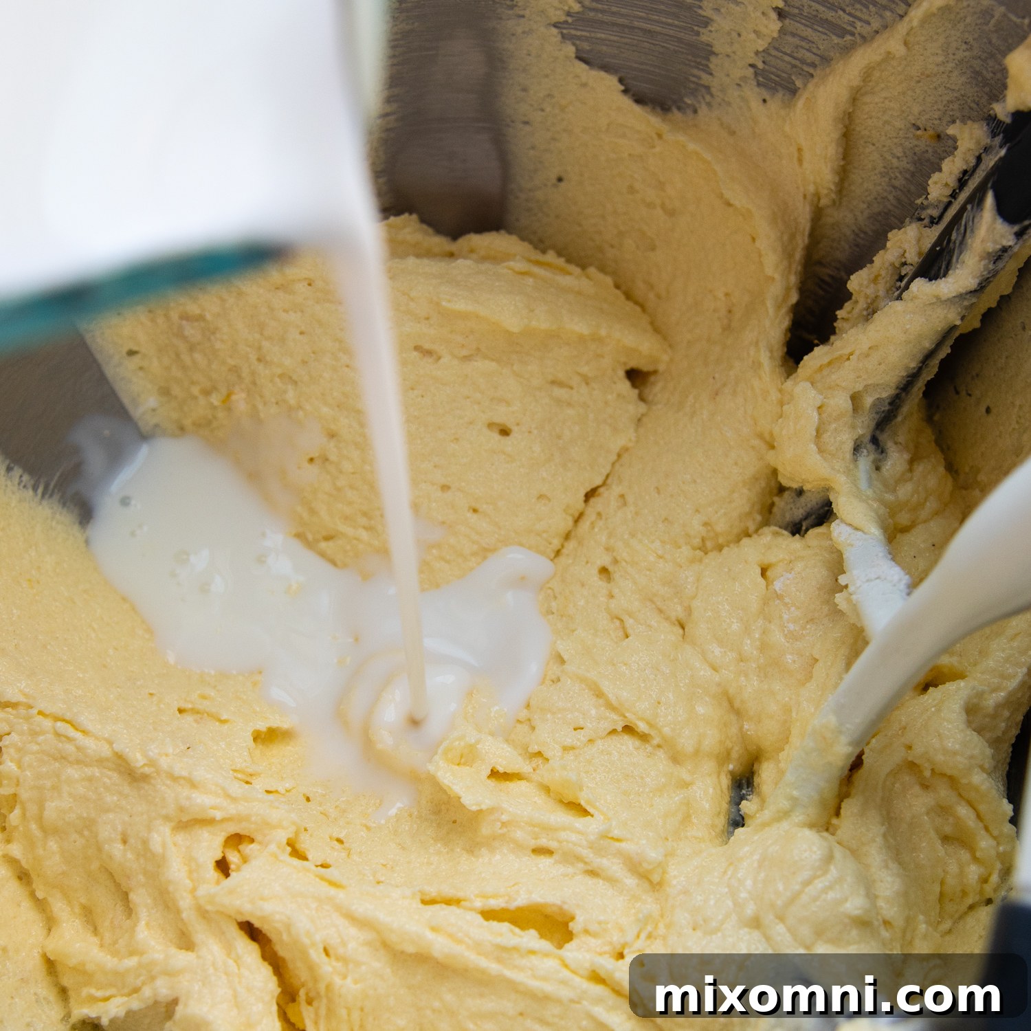 Canned coconut milk being poured into the cake batter, demonstrating the alternating method of adding ingredients.
