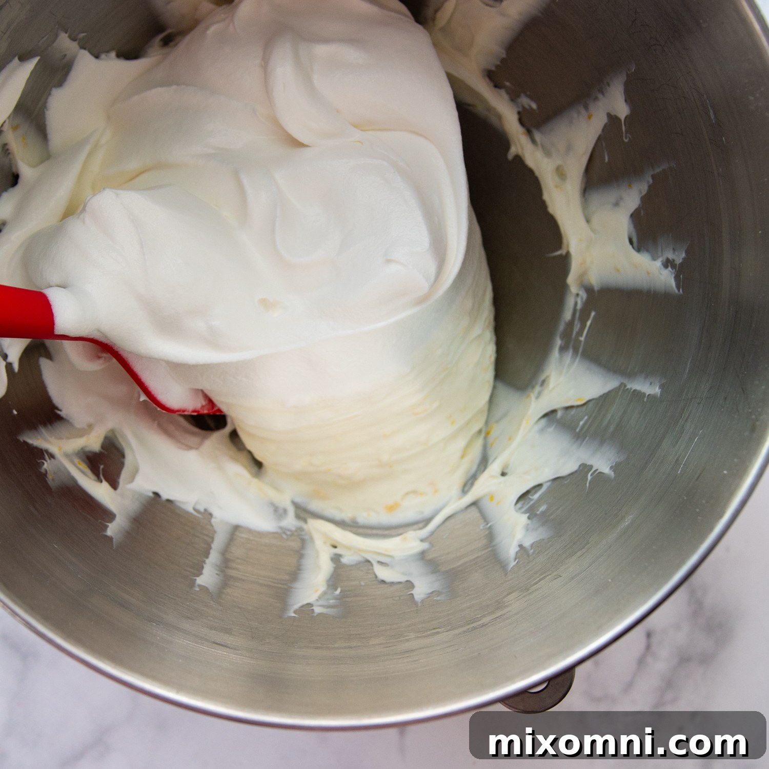 Cool Whip whipped topping being folded into a creamy lemon cream cheese frosting base, creating an airy texture.