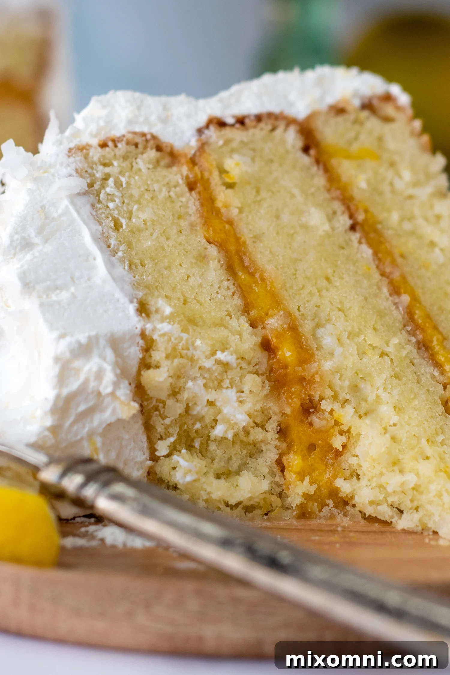 Close-up of a bitten slice of gluten-free coconut lemon cake on a rustic wooden plate, showing the fluffy layers and lemon curd filling.