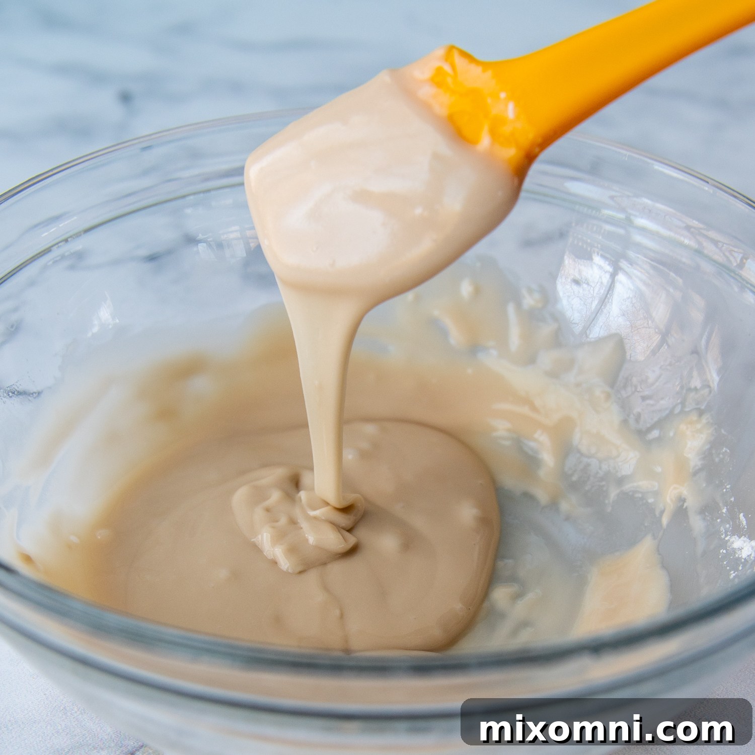 A yellow spoon lifts dripping vanilla glaze to demonstrate its perfect consistency for drizzling over coffee cake.