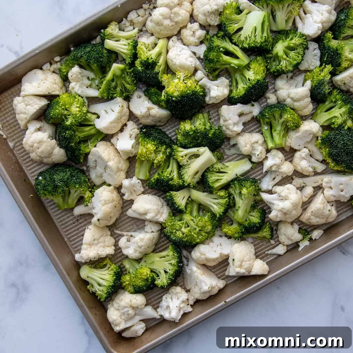 Fresh broccoli and cauliflower florets evenly spread on a baking sheet, ready for roasting.