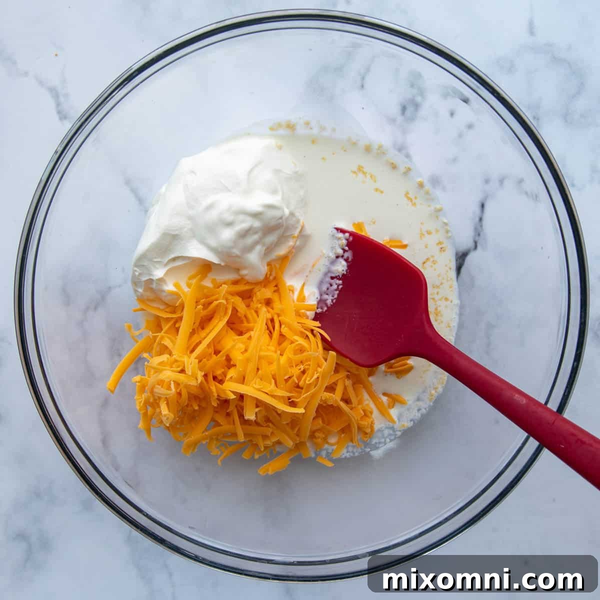 Ingredients for the creamy cheese sauce, including sour cream, heavy cream, shredded cheddar, and garlic powder, in a mixing bowl.