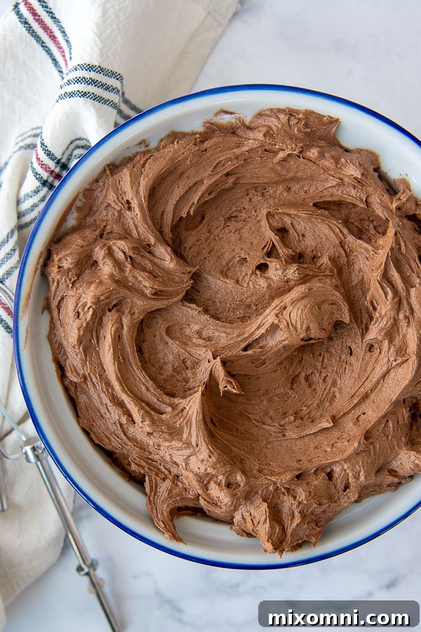 Overhead shot of rich, fluffy chocolate frosting in a white mixing bowl, ready for decorating.