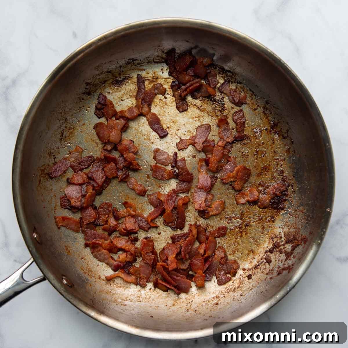 Chopped bacon sizzling in a large skillet, ready to be cooked until crisp.