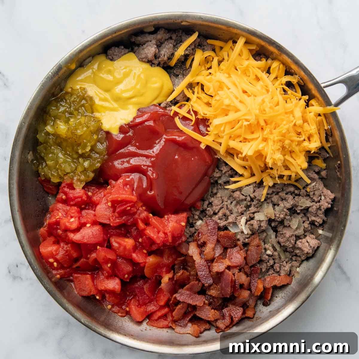 Ground beef and diced onions browning in a skillet with cheeseburger sauce ingredients like ketchup, mustard, and relish nearby.