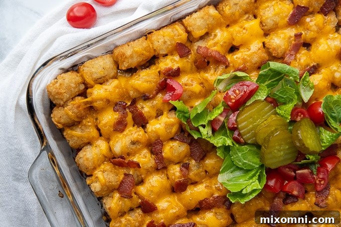 Close-up, top-down view of a serving of cheeseburger casserole, garnished with fresh shredded lettuce, sliced pickles, and chopped tomatoes.