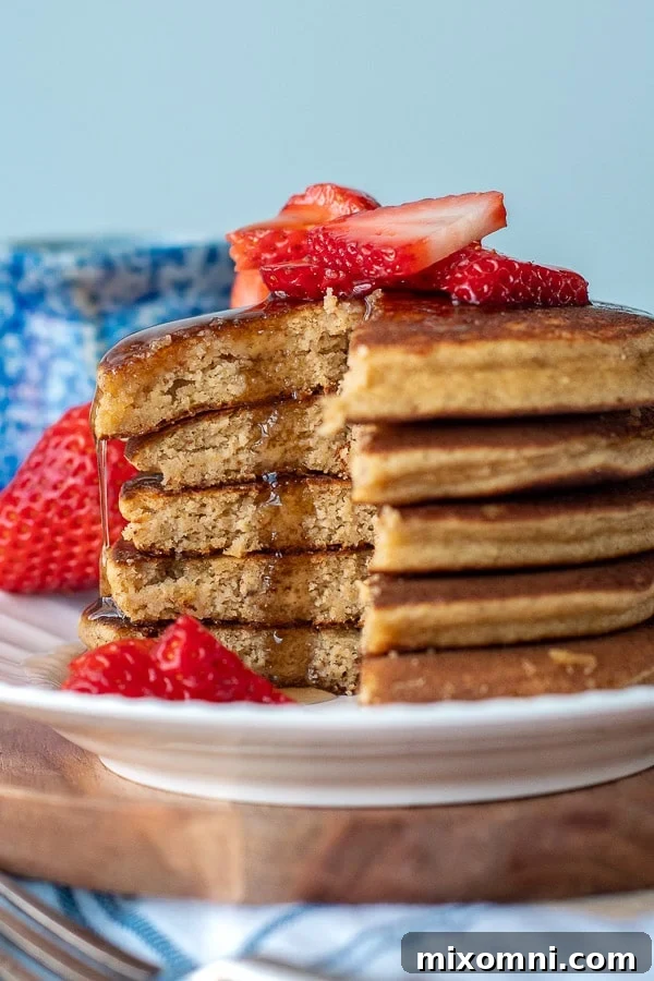 A stack of golden brown almond flour banana pancakes, artfully cut, with warm maple syrup cascading down the sides. Fresh fruit and a pat of butter could be nearby, enhancing the inviting scene.