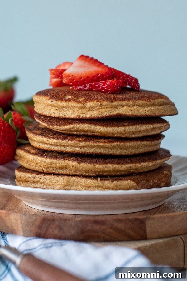 A beautifully plated stack of almond flour pancakes on a white plate, adorned with vibrant, freshly sliced strawberries. The arrangement highlights the appetizing texture and inviting color of the breakfast.