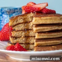 A stack of golden almond flour banana pancakes, with a slice already cut, and maple syrup drizzling down, indicating a delicious, ready-to-eat breakfast.