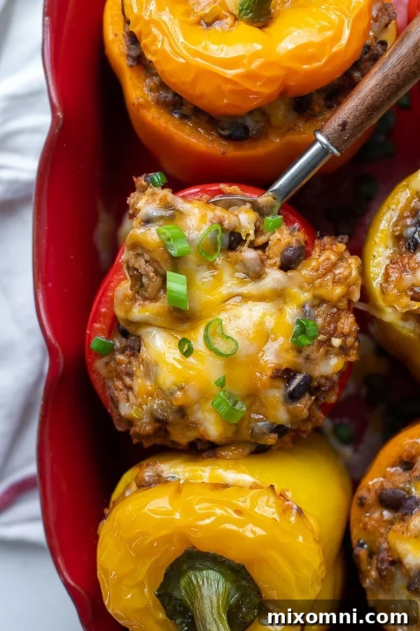 Overhead shot of vibrant Mexican stuffed peppers arranged neatly in a baking dish, with a serving spoon gently scooping into one, showcasing the melted cheese and hearty filling.