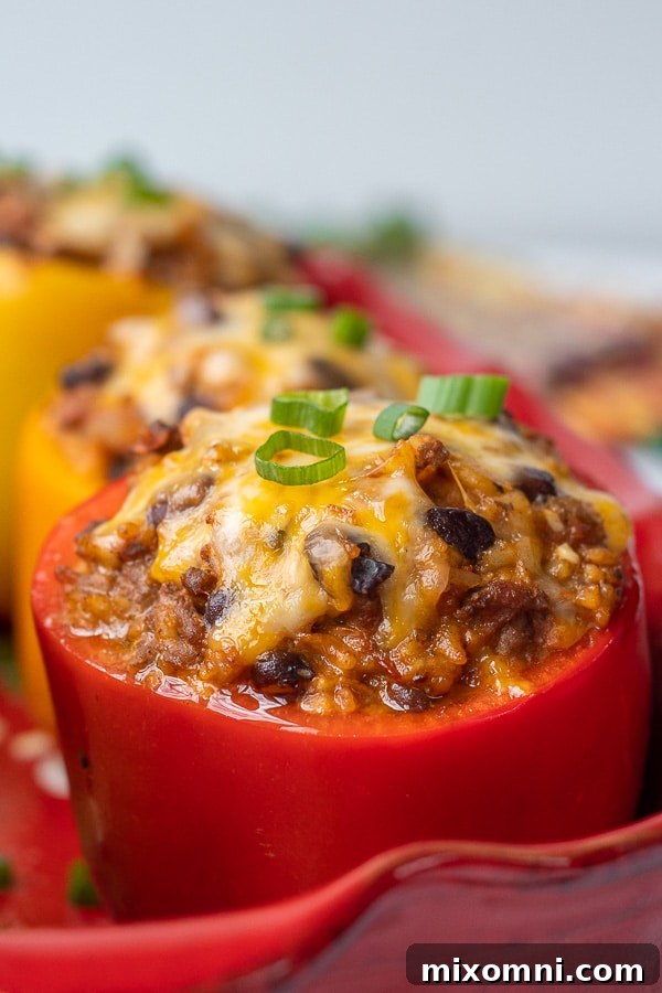 Close-up side angle shot of a single Mexican stuffed bell pepper in a baking dish, showing the beautifully melted, golden, and bubbly cheese topping. The rich filling is visible beneath.