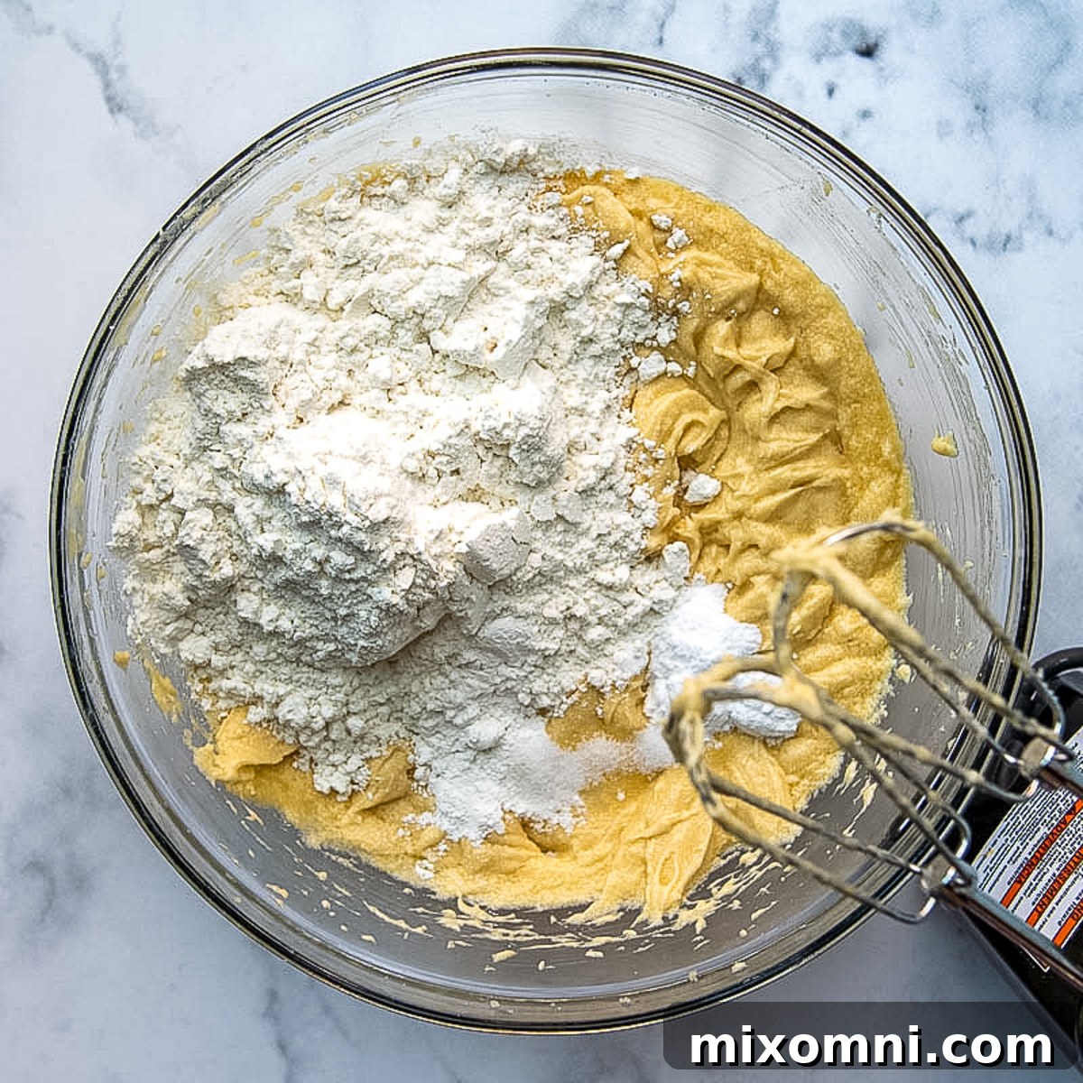 All-purpose flour being added to the cake batter in a mixing bowl.