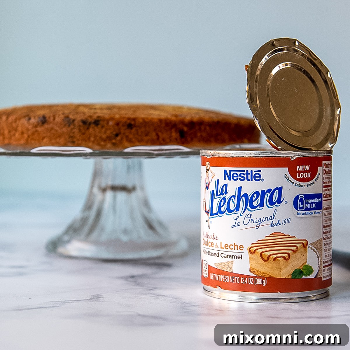 A can of dulce de leche in the foreground, with cake layers being assembled in the background.