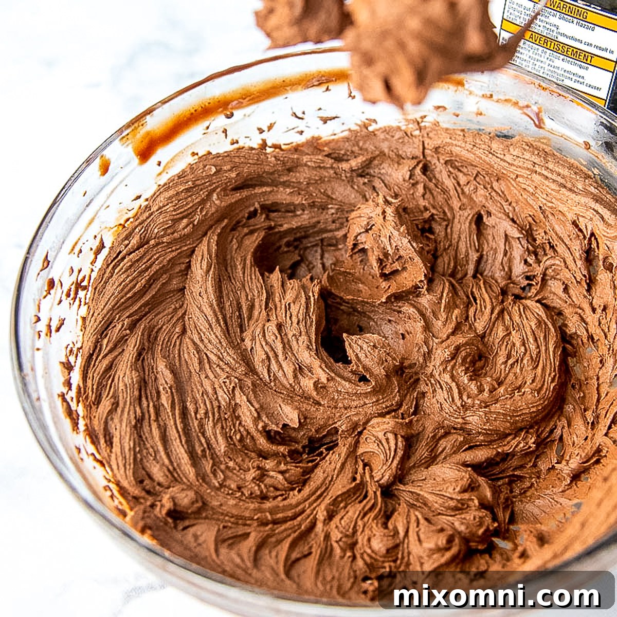 Light and fluffy whipped chocolate ganache frosting in a clear glass mixing bowl.