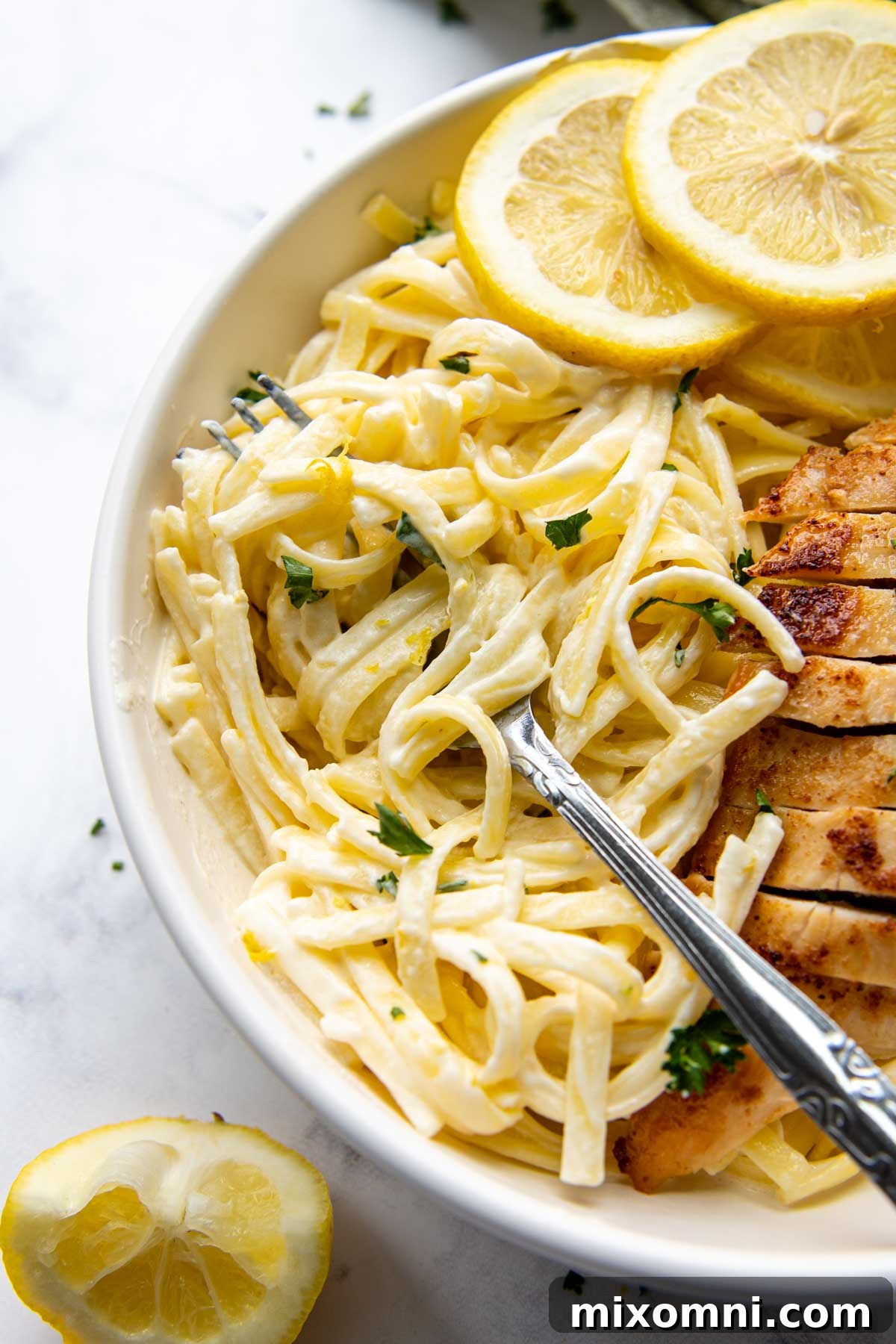 a fork going into a pasta in a bowl with lemon slices garnishing the dish.