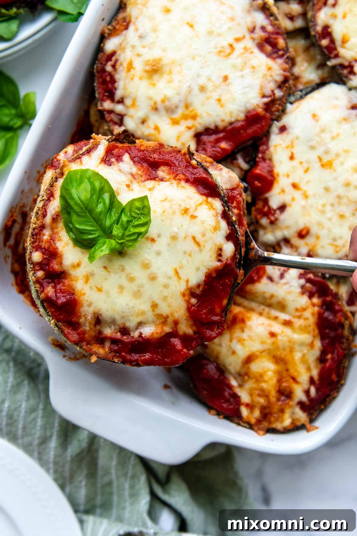 a spatula holding up a serving of gluten-free eggplant parmesan with fresh basil on top