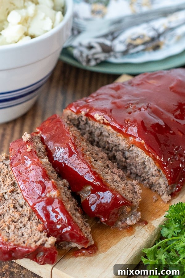 instant pot meatloaf sliced on a wooden board with a bowl of mashed potatoes in the background