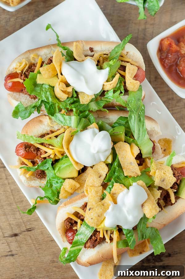 an overhead shot of mexican hot dogs on a white rectangle plate with a small dish of salsa next to it