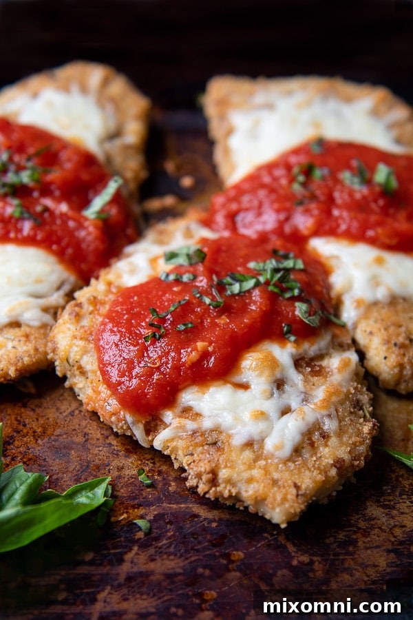 a close up of parmesan chicken on a baking sheet with sauce and cheese on top