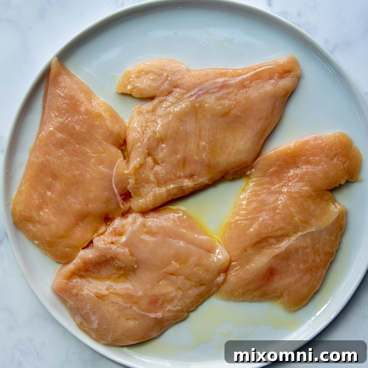 chicken cutlets on a plate with oil drizzled on.