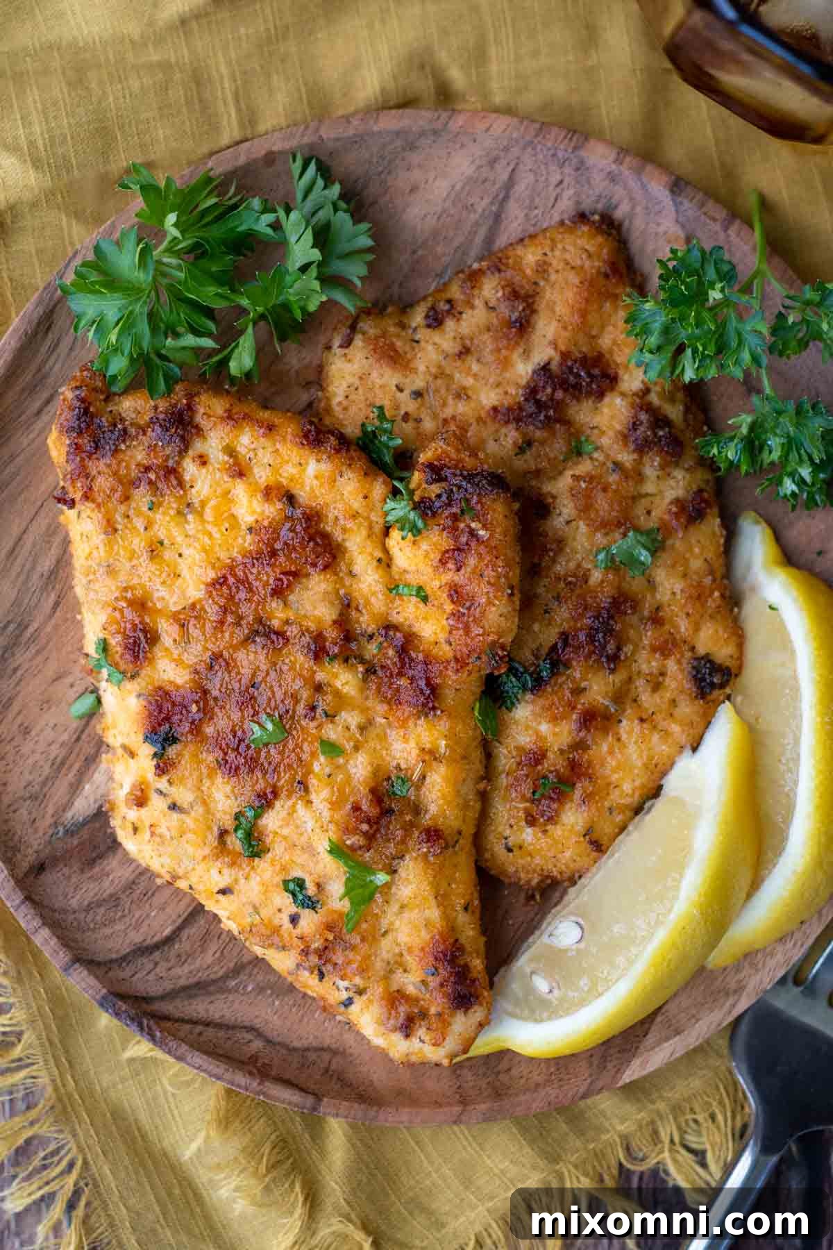 bread chicken cutlets on a wood plate with parsley and lemon