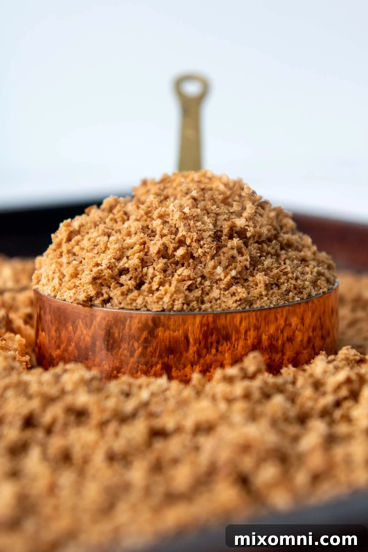 A heaping scoop of golden brown, homemade gluten-free breadcrumbs in a copper measuring cup, ready for use.