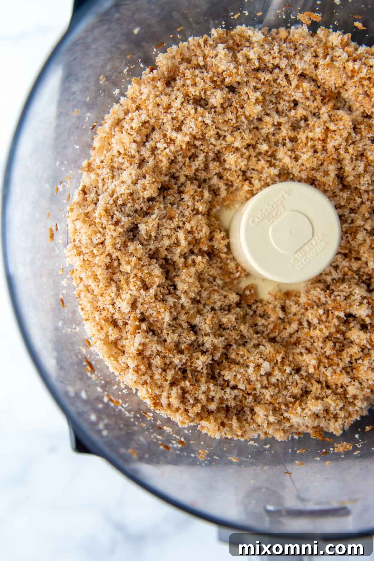 An overhead shot of coarse gluten-free breadcrumbs in a food processor bowl, illustrating the processing stage.