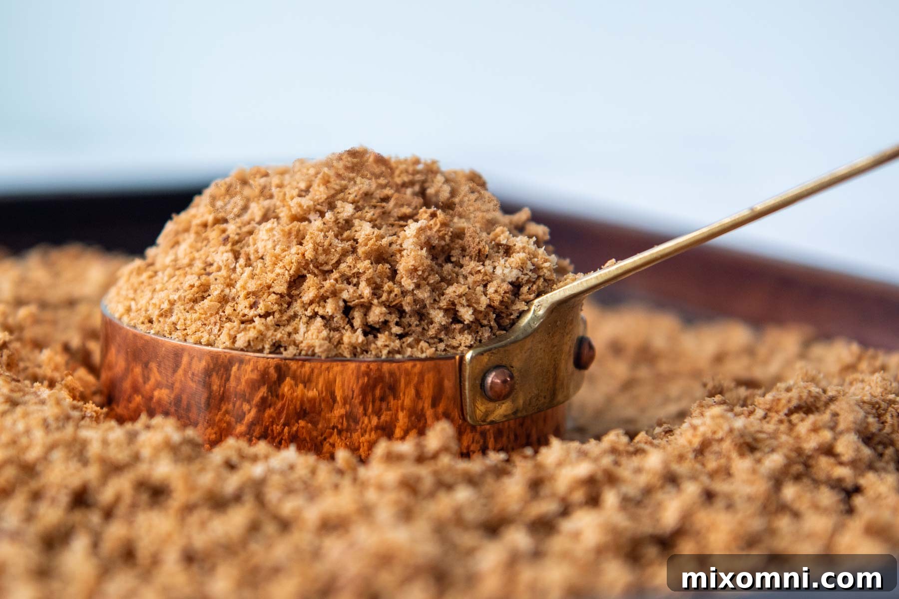 A copper measuring cup filled with golden, toasted homemade gluten-free breadcrumbs, showcasing their appealing texture.