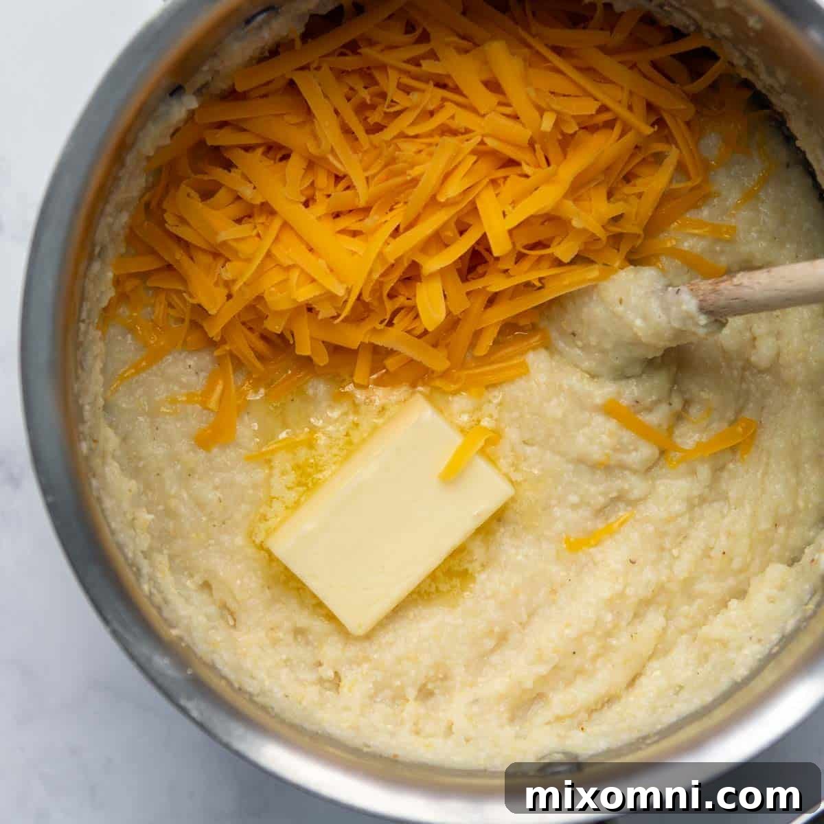 Melted butter and shredded cheddar cheese being stirred into cooked grits.