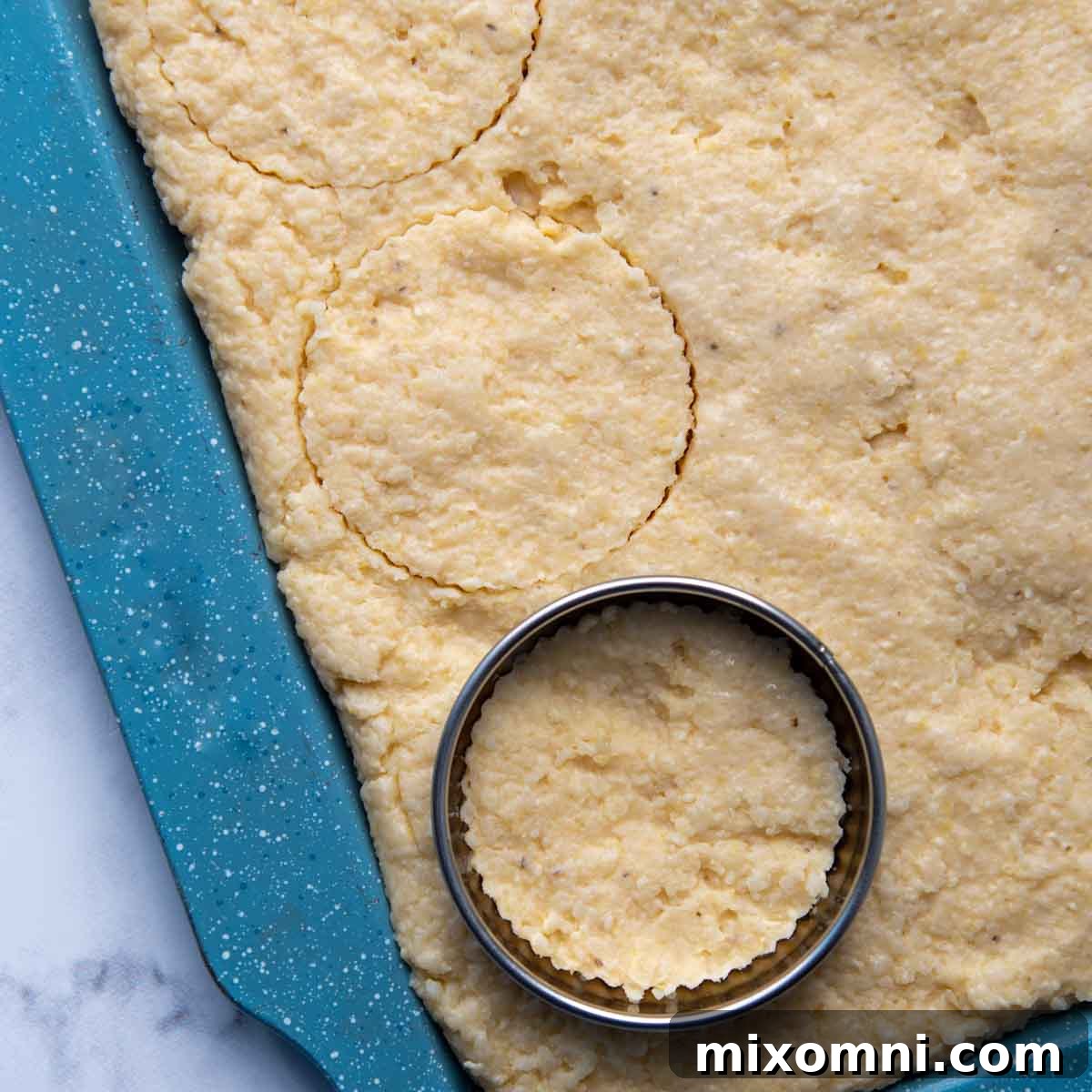 A pan of cooled, firm grits with a round biscuit cutter being used to cut out a circular grit cake.