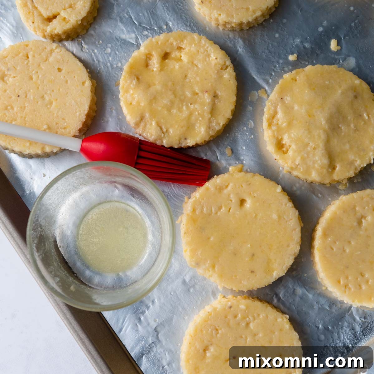 Grit cakes arranged on a baking sheet, brushed with melted butter, ready for broiling.