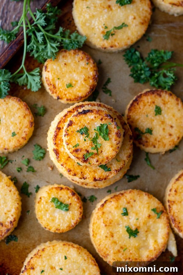 Overhead shot of freshly broiled grit cakes on a baking sheet, with fresh parsley scattered around.