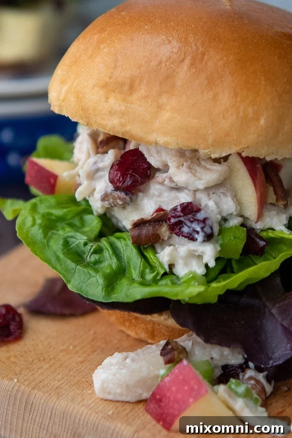 A delicious cranberry pecan chicken salad sandwich on a brioche bun, artfully presented on a rustic wooden cutting board.