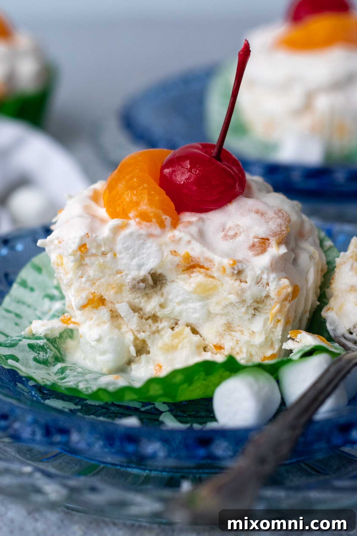 A vibrant frozen fruit salad cup, partially eaten, rests on a blue plate, with a spoon beside it.