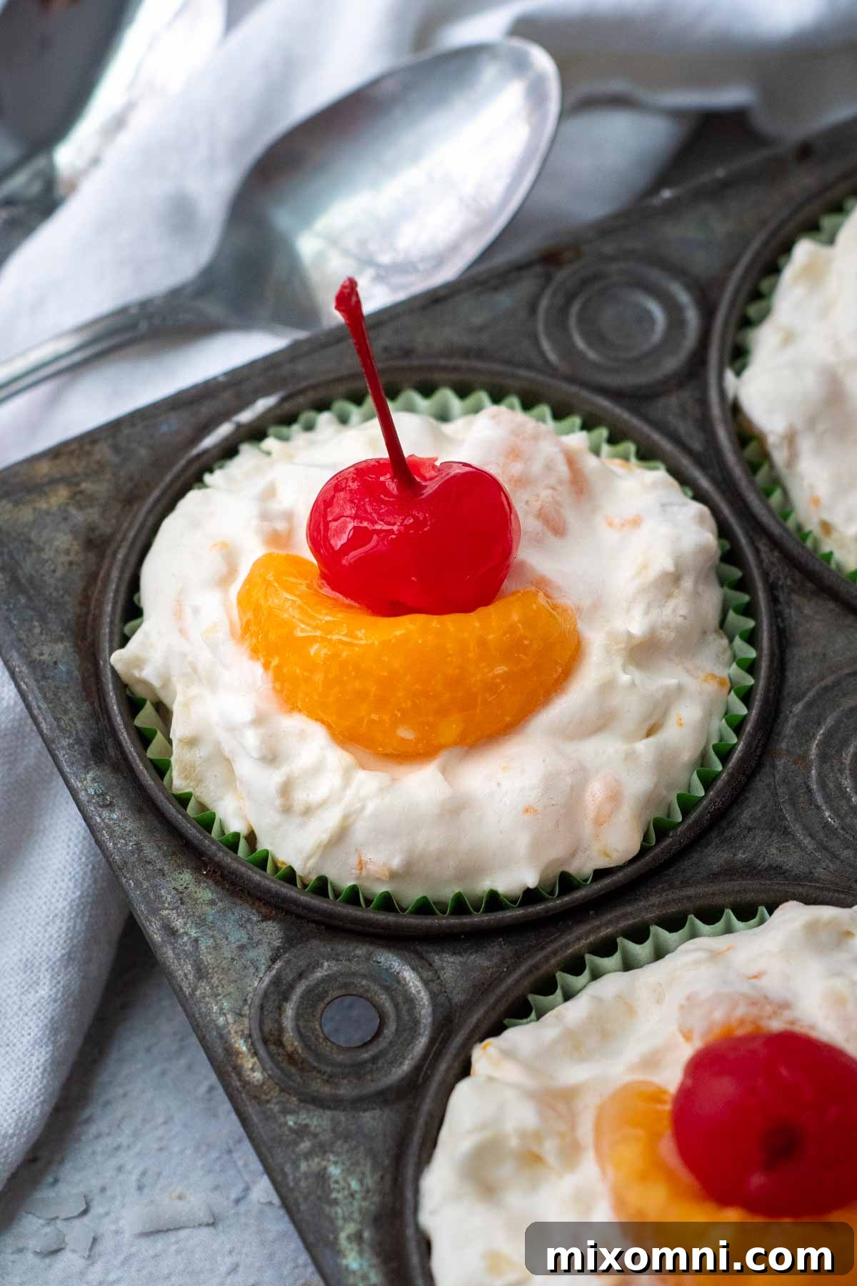 Top view of frozen fruit salad cups neatly arranged in a muffin tin, garnished with orange segments and cherries.