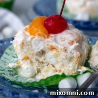 A frozen fruit salad cup on a blue plate with a bite taken out and spoon resting next to it