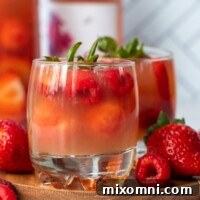 A close-up of sparkling rose sangria in a glass, garnished with fresh berries and citrus slices, on a rustic wooden surface.