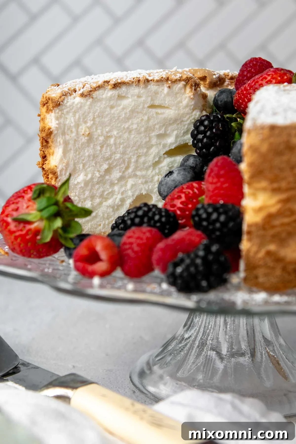 A beautifully sliced gluten-free angel food cake on a stand, adorned with fresh berries.