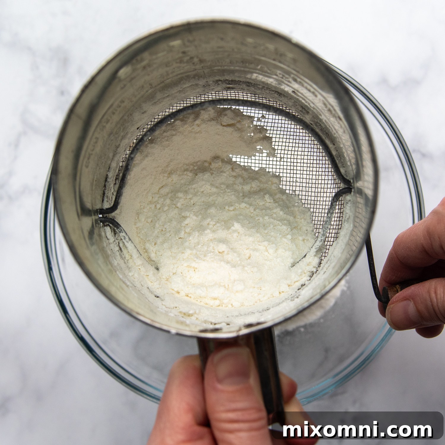 Dry ingredients being sifted with a sifter into a bowl.