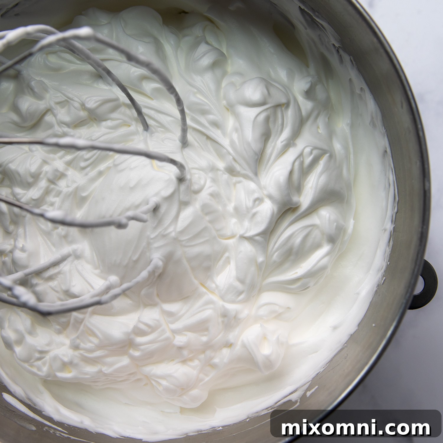 Glossy meringue being mixed in a large bowl.