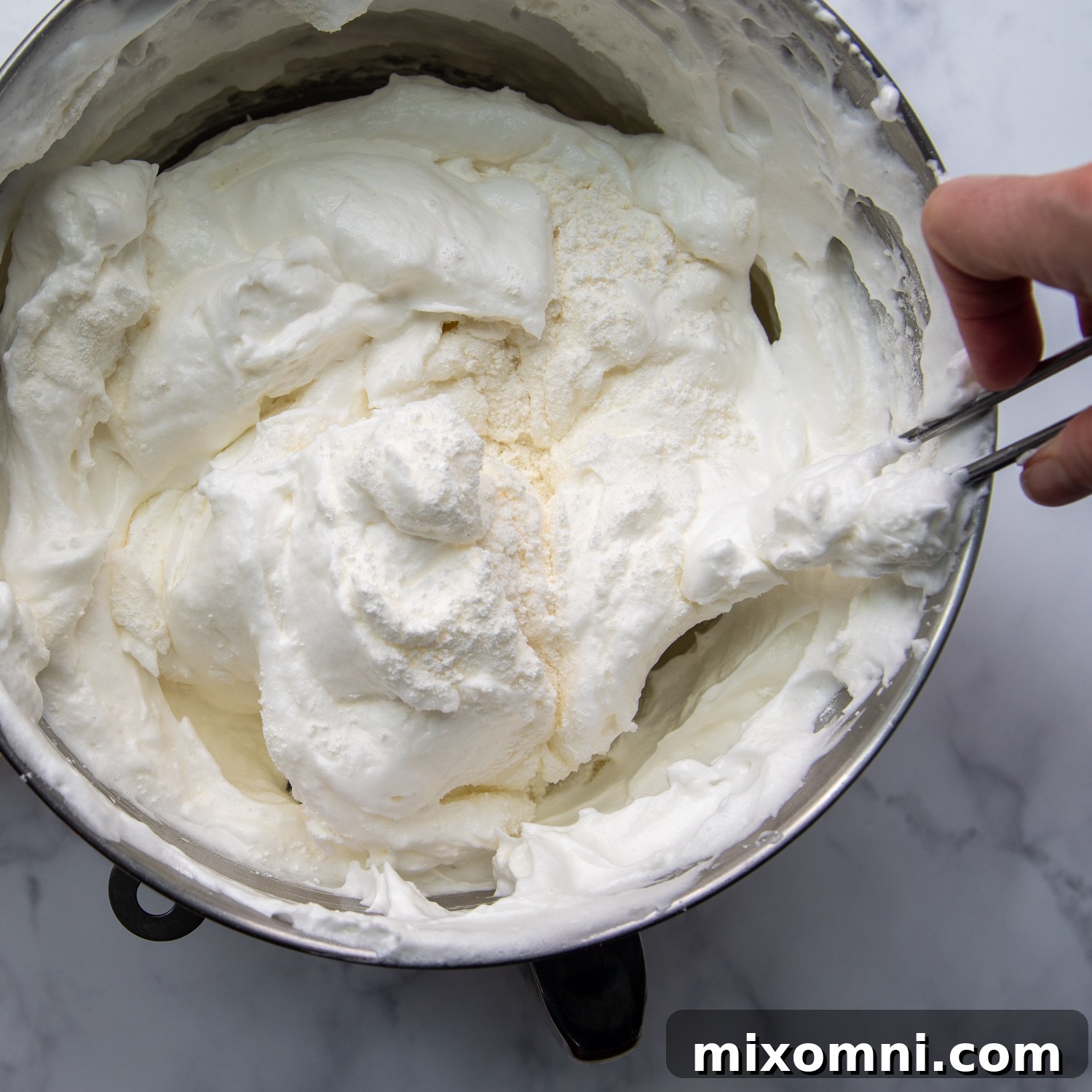 Dry ingredients being gently folded into the meringue with a spatula.