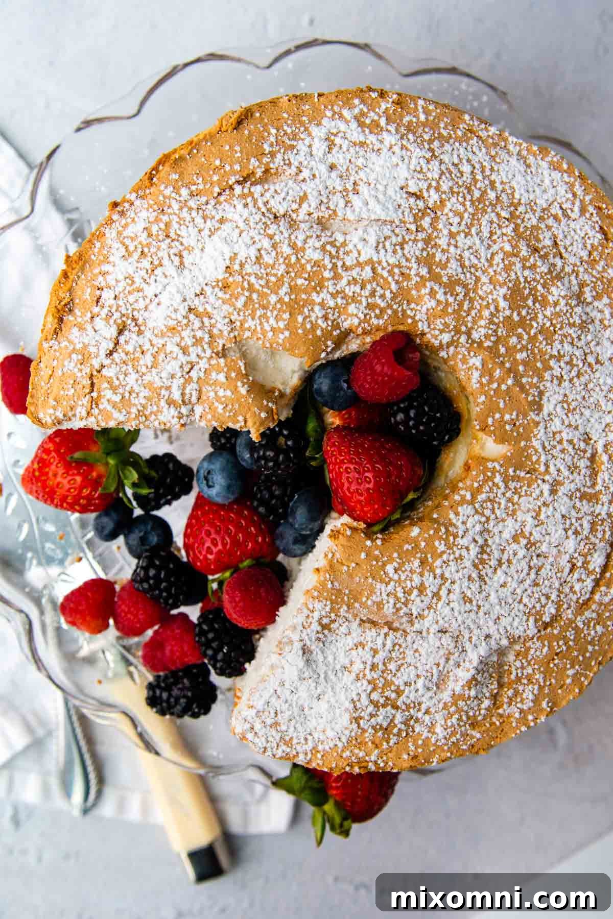 An overhead shot of a beautiful angel food cake with fresh berries in the center, alongside a cake knife.