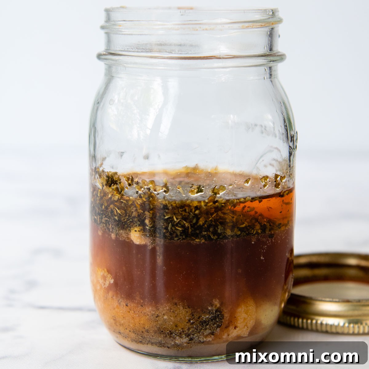 A glass jar filled with a vibrant orange-red sun-dried tomato dressing, ready to be shaken and poured over the pasta salad.